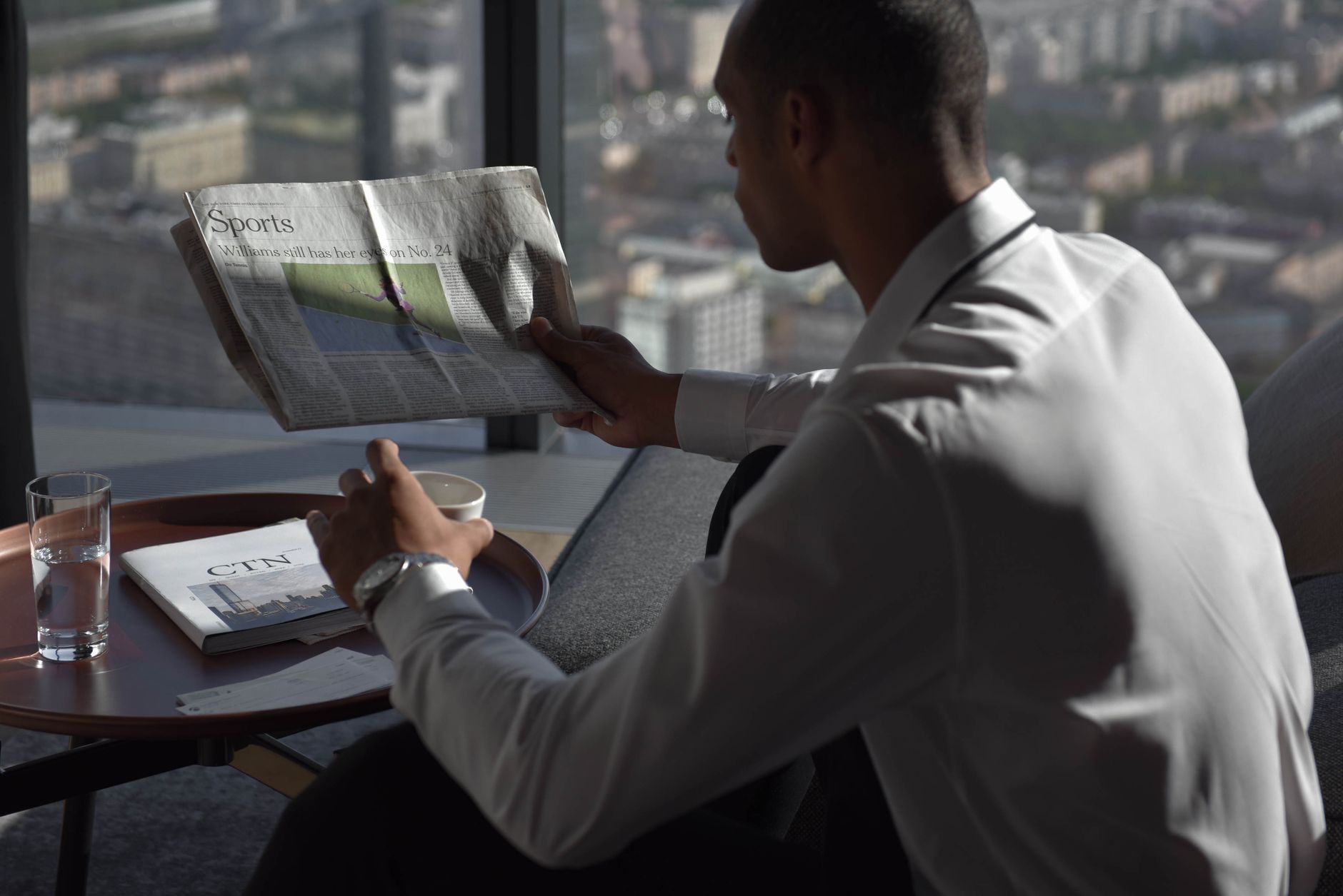 Businessman in office reading sports section, enjoying coffee with city view. — Content Review 712-290142-446a547720de