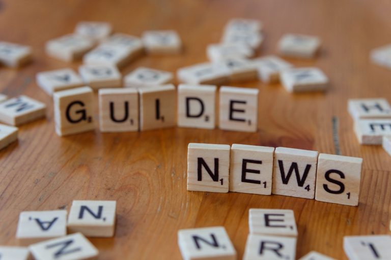 Close-up of Scrabble tiles spelling 'Guide' and 'News' on a wooden surface. — Golden Pharaoh Casino: Ein Blick hinter die Kul