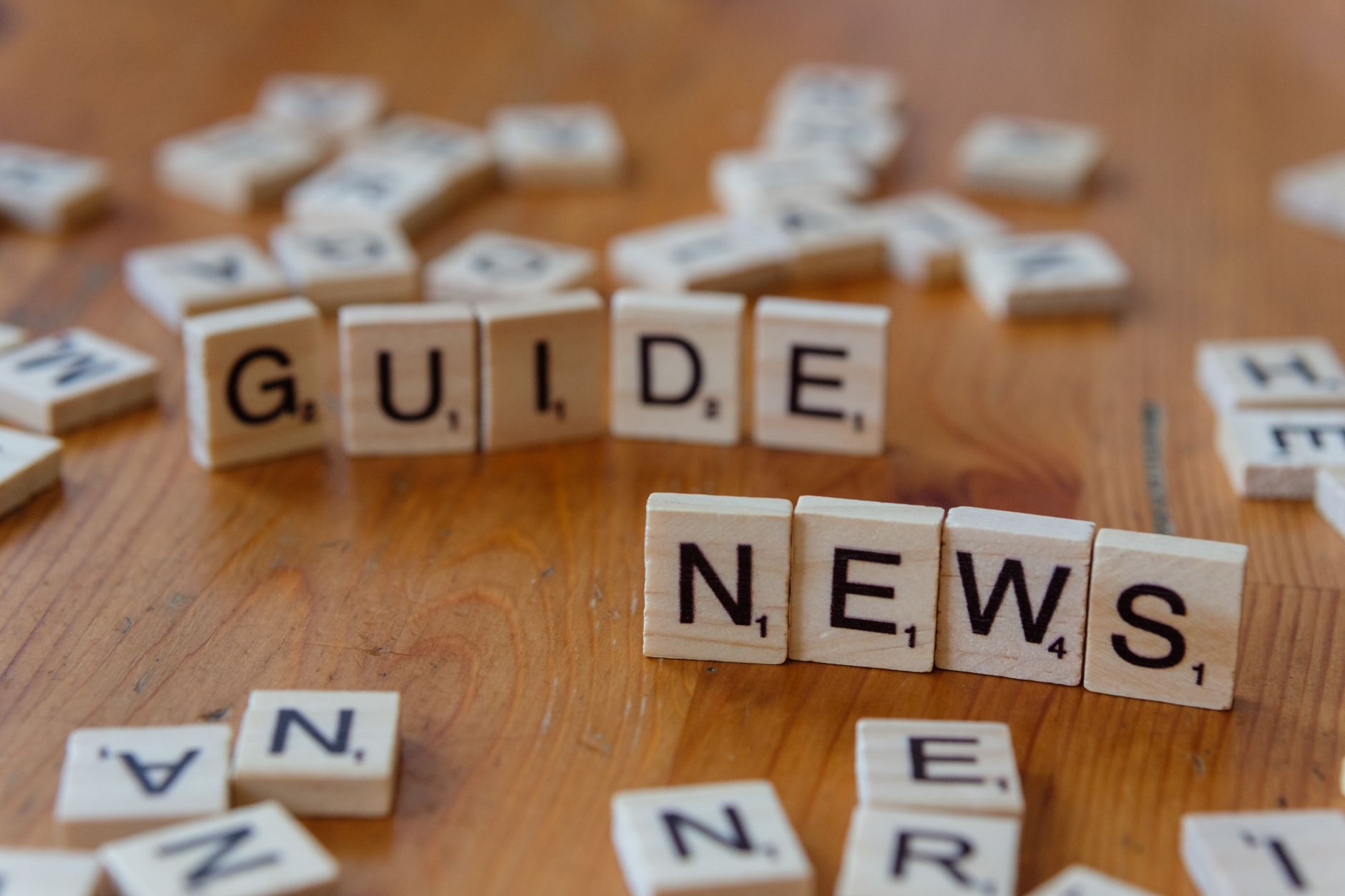 Close-up of Scrabble tiles spelling 'Guide' and 'News' on a wooden surface. — Golden Pharaoh Casino: Ein Blick hinter die Kul