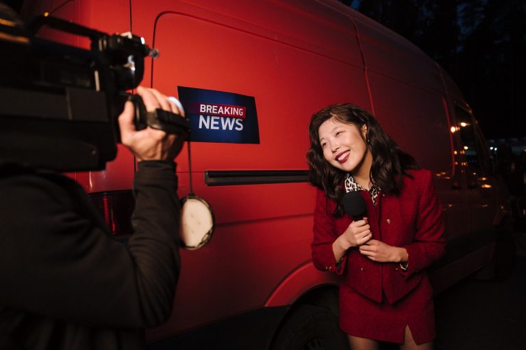 Asian female reporter in a red blazer reporting live on the news outdoors in the evening. — Thor Casino et ses offres promoti